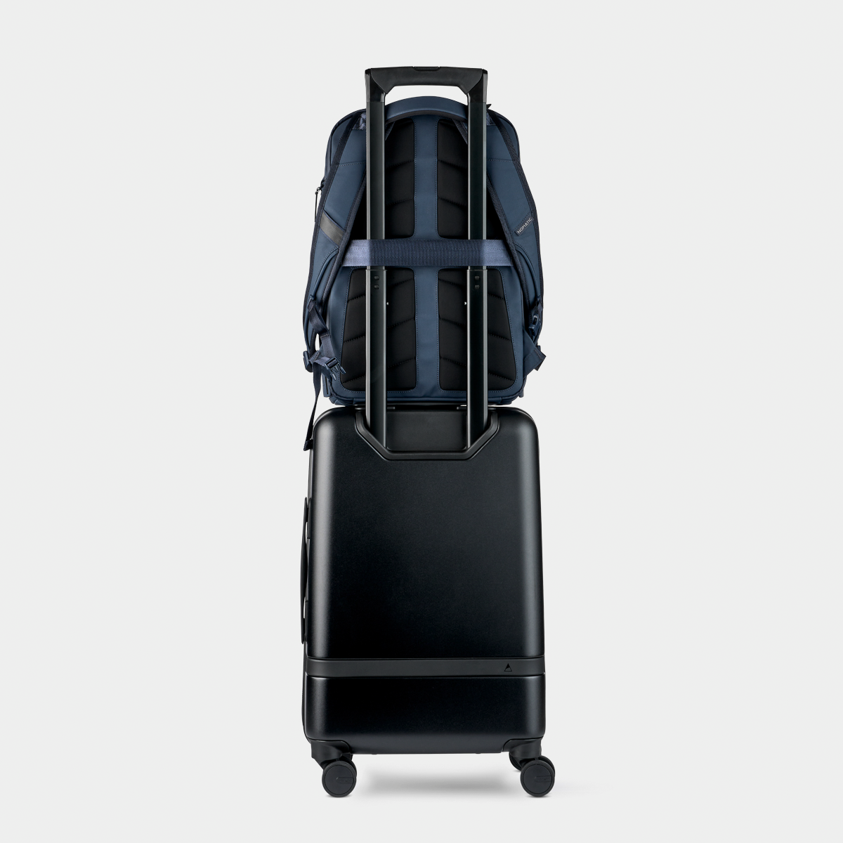 Black suitcase with a blue backpack on top against a light gray background