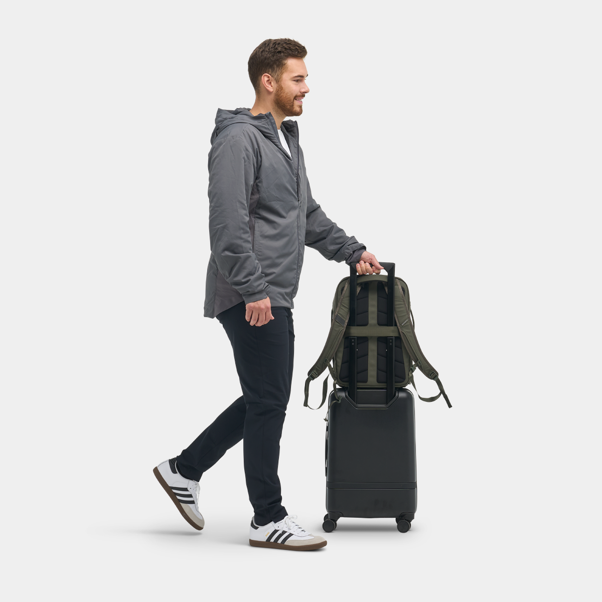 Nomatic Travel Pack 14L olive on model showing backpack on top of luggage with luggage pass through carry option